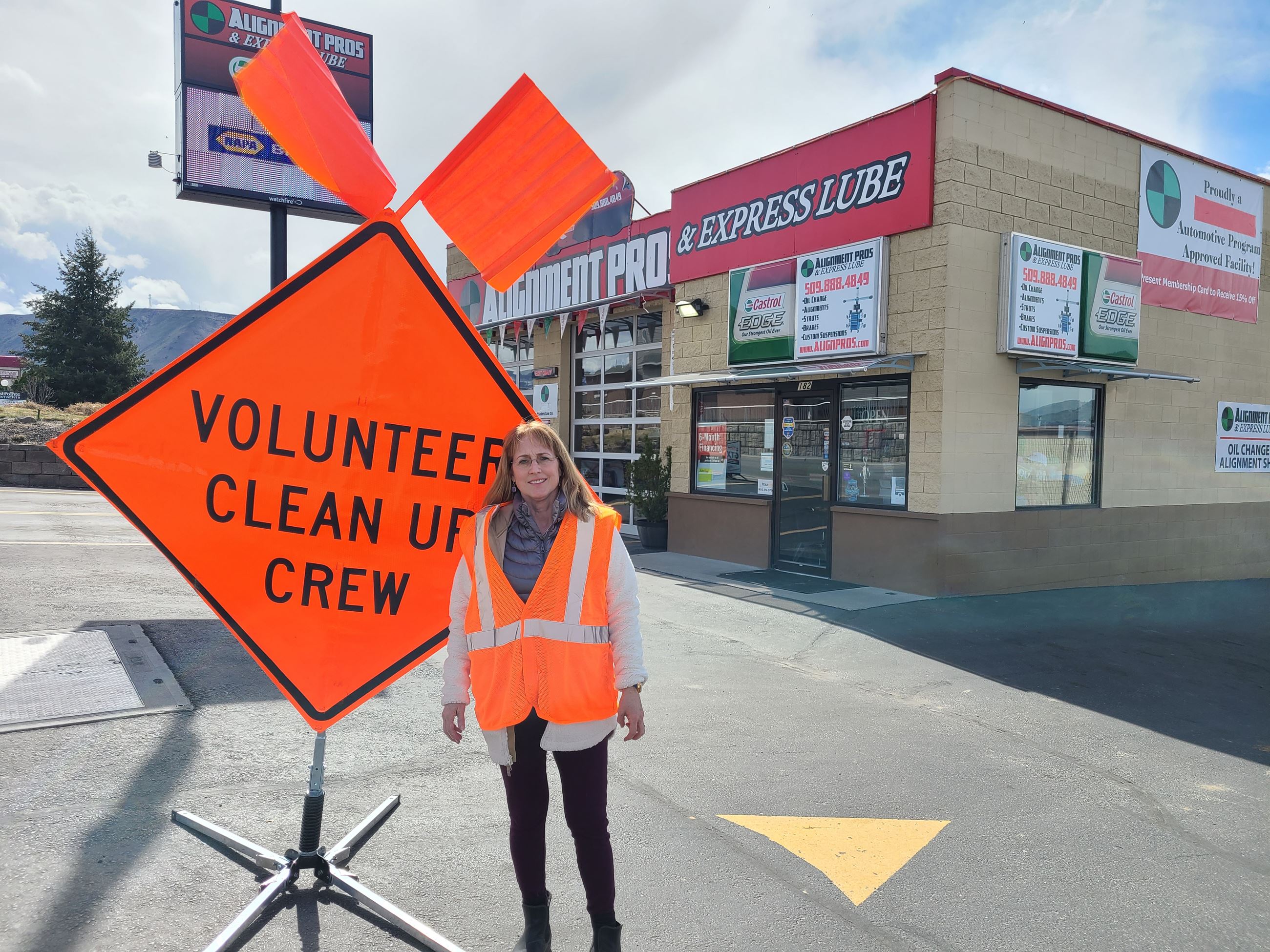 A woman stands next to a large orange sign that says "Volunteer clean up crew"