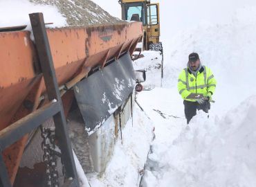 A man stands next to a snowplow and snowpile