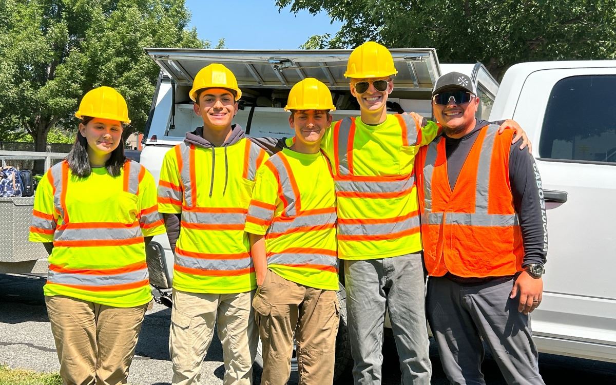 Four teens and an adult team lead where reflective vests and hardhats while standing near a truck