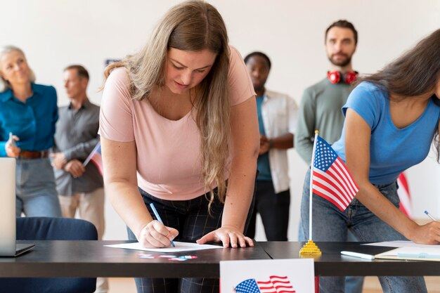 Two women in the foreground are writing on voter registration forms at a table.